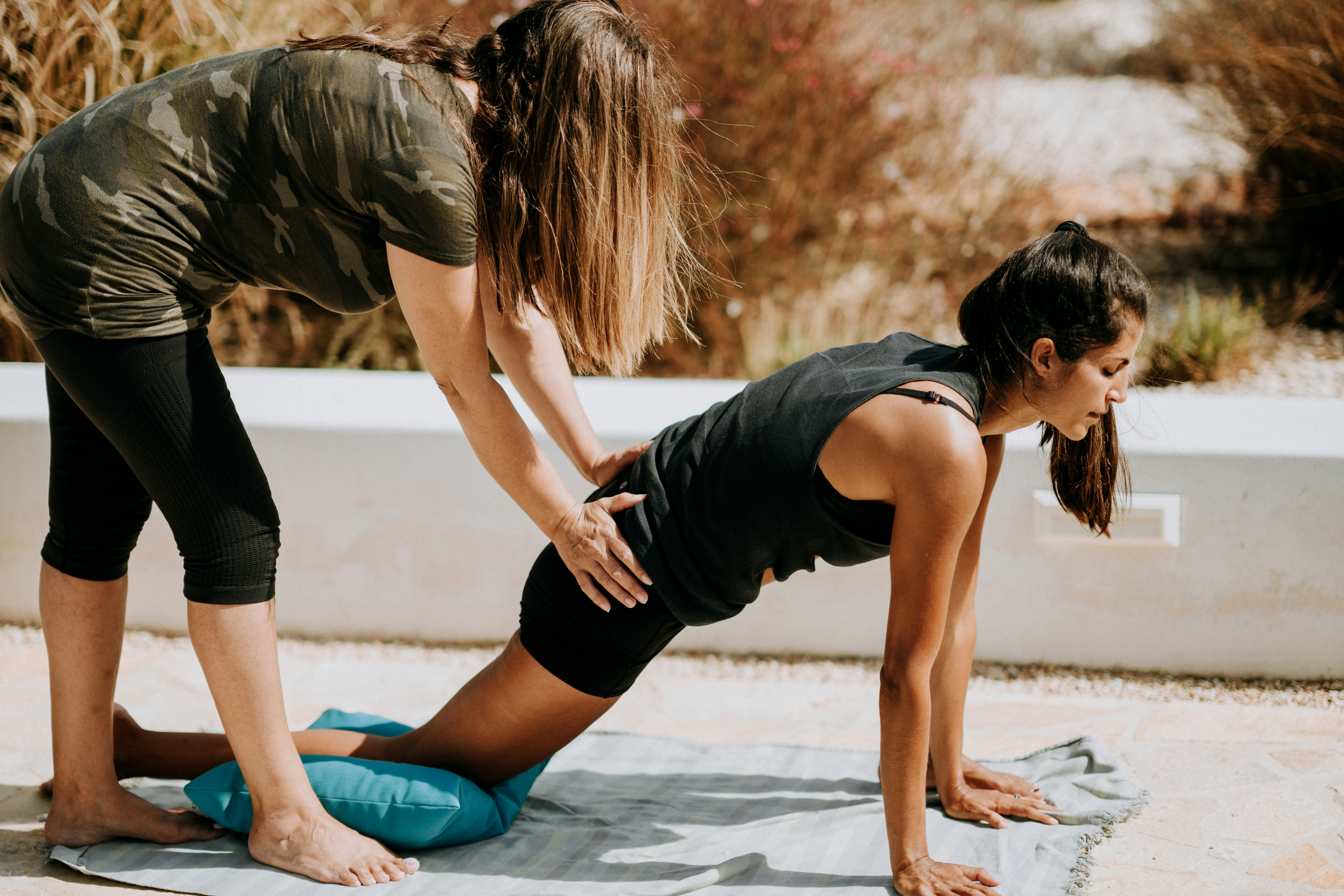 A woman helping another woman with a yoga pose
